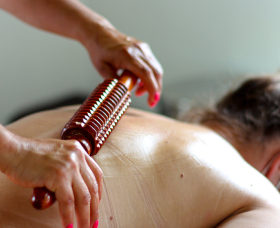A person receiving a back massage with a wooden roller tool.