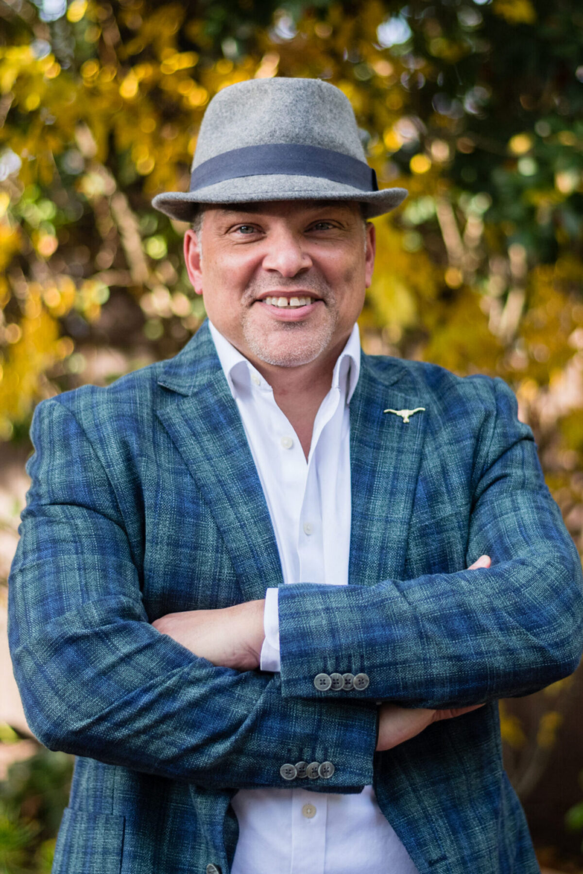 a man in a blue plaid blazer and gray hat outdoors.
